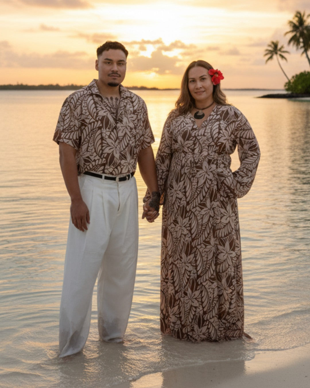 Couple in matching outfits standing in water at sunset on a beach.