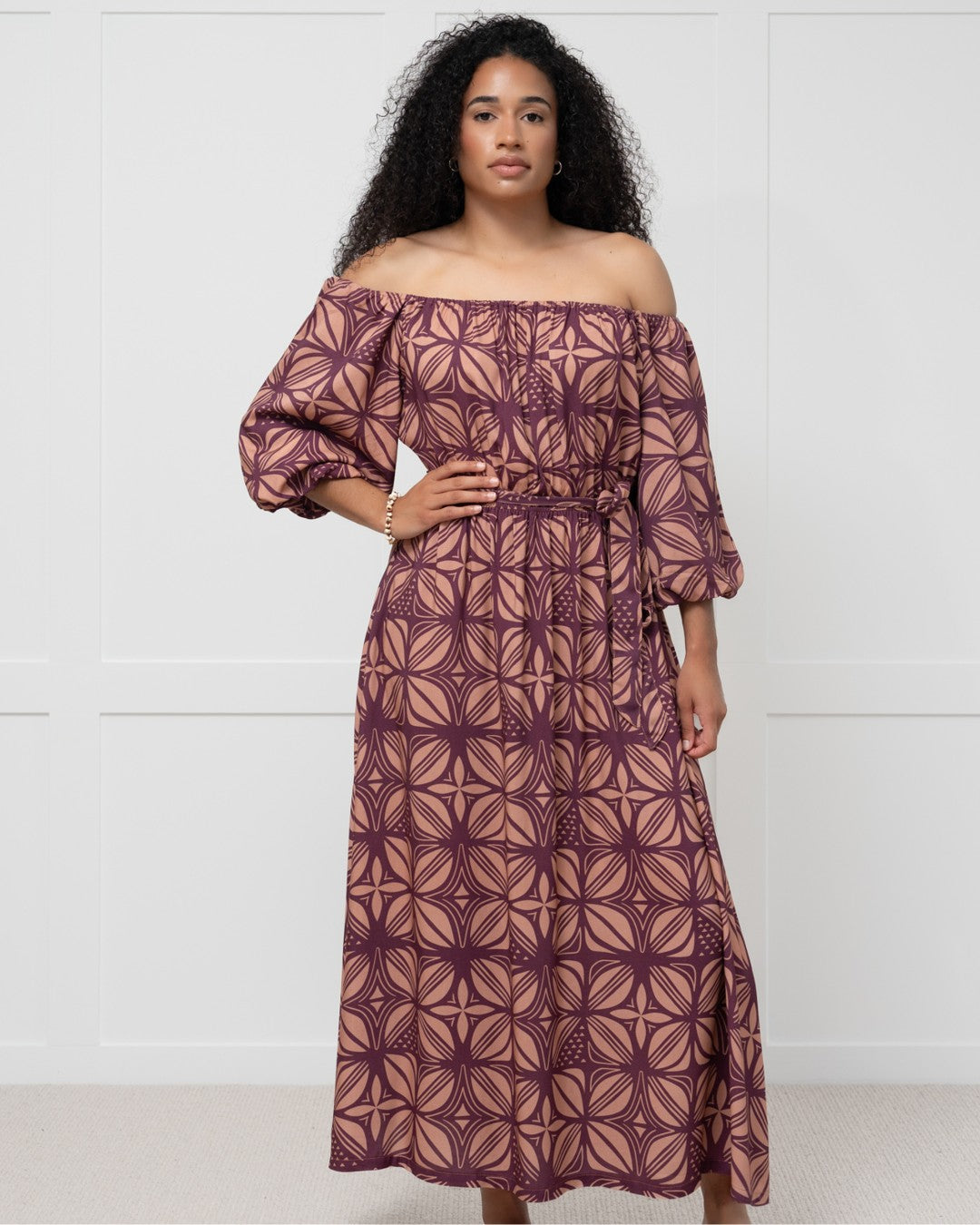 Woman wearing a patterned island dress against a white wall