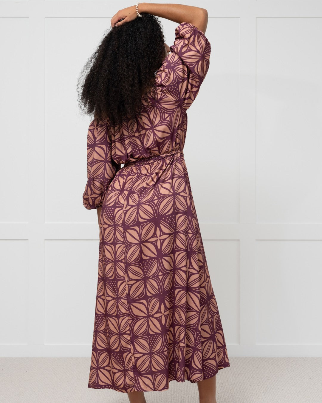 Woman wearing a patterned island dress against a white wall
