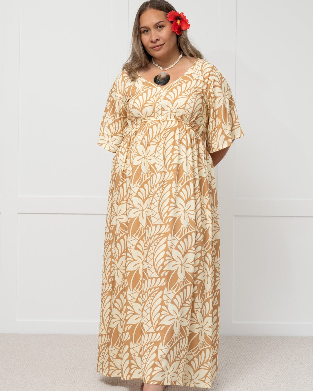 Woman wearing a long, patterned island dress against a white background