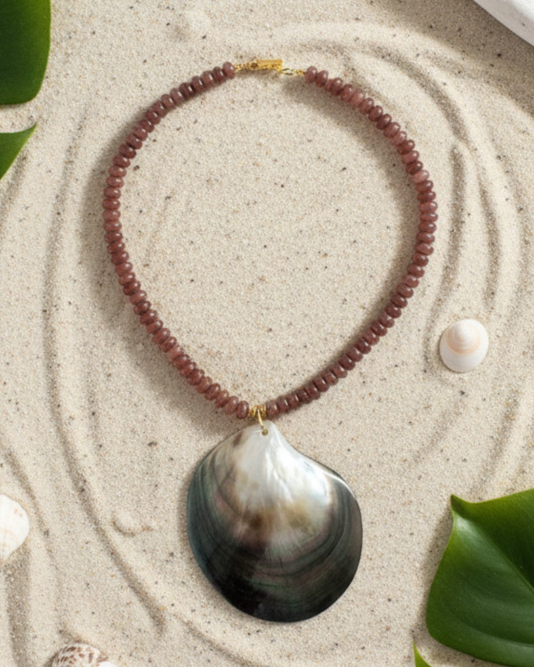 Necklace with a large shell pendant on a sandy surface with leaves