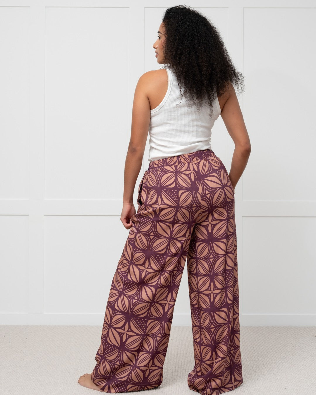 Woman wearing a white top and patterned purple island pants against a white background