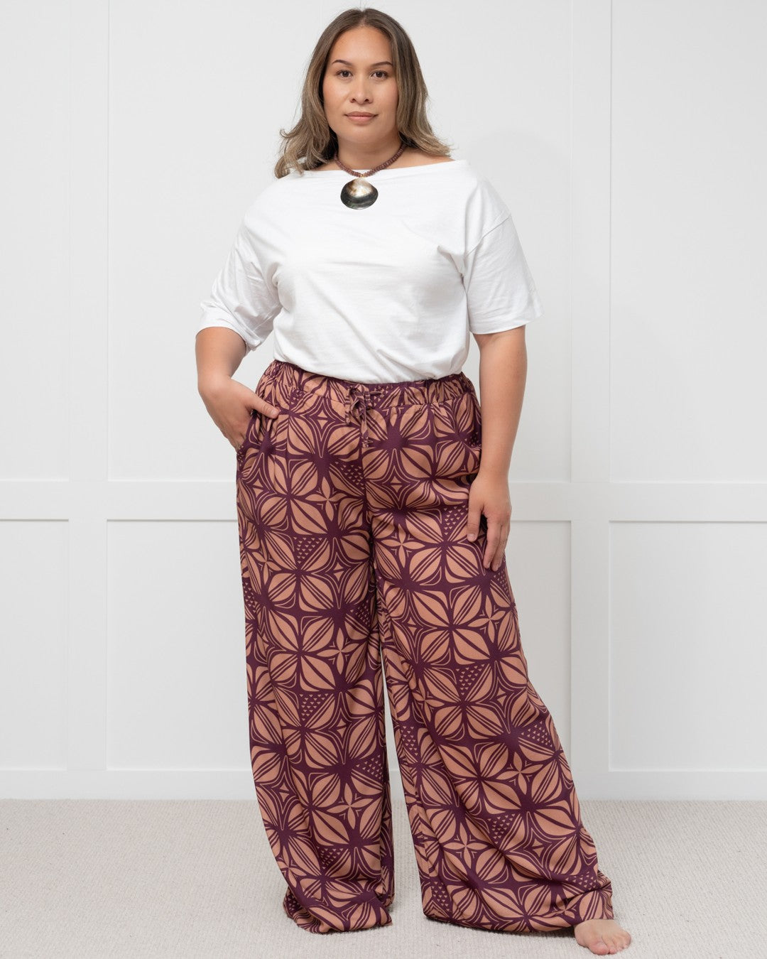 Woman wearing a white top and patterned purple island pants against a white background