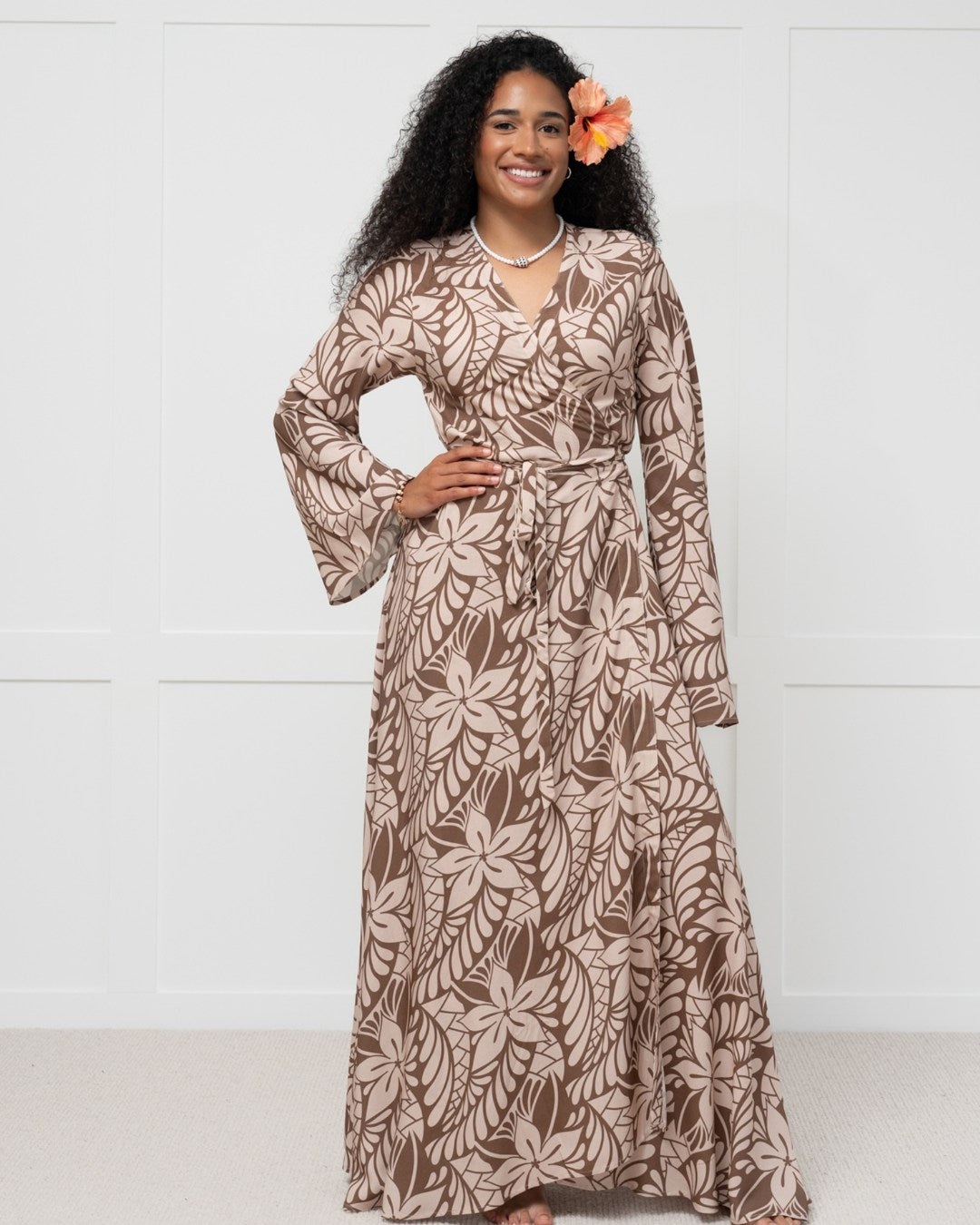 Woman wearing a long brown floral island dress against a white background