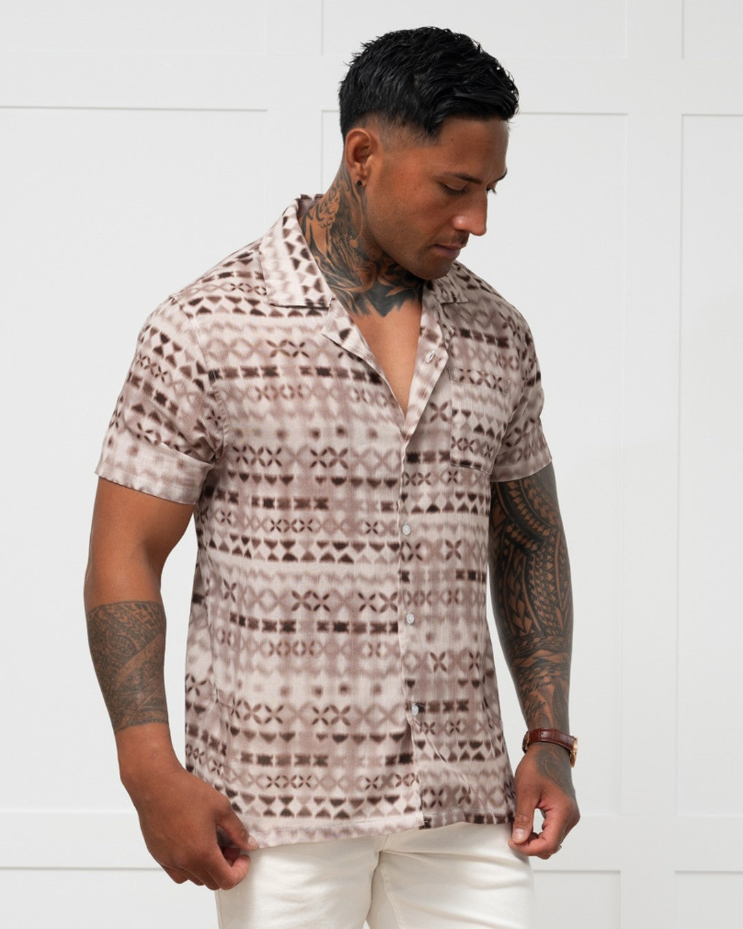 Man standing against a white wall wearing a polynesian motif mens island shirt