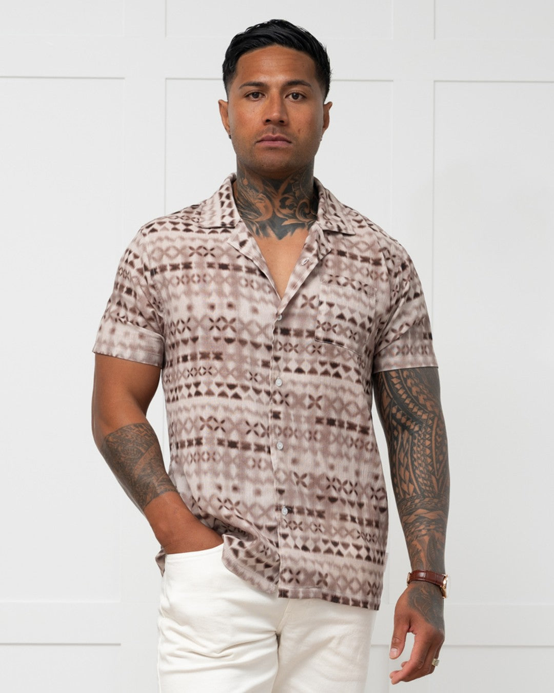 Man standing against a white wall wearing a polynesian motif mens island shirt