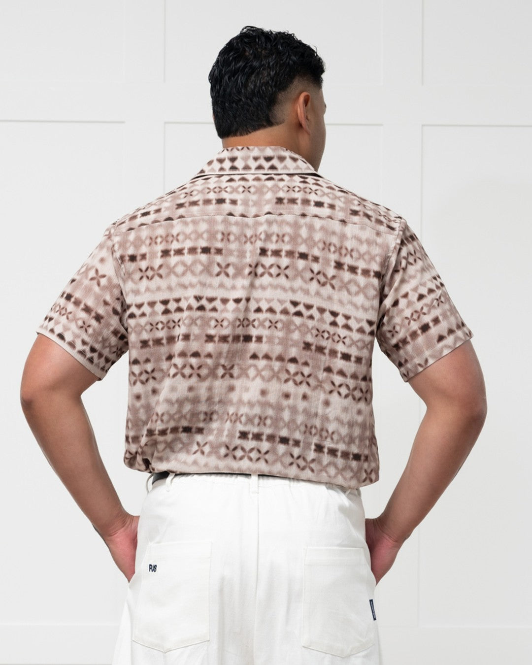 Man standing against a white wall wearing a polynesian motif mens island shirt