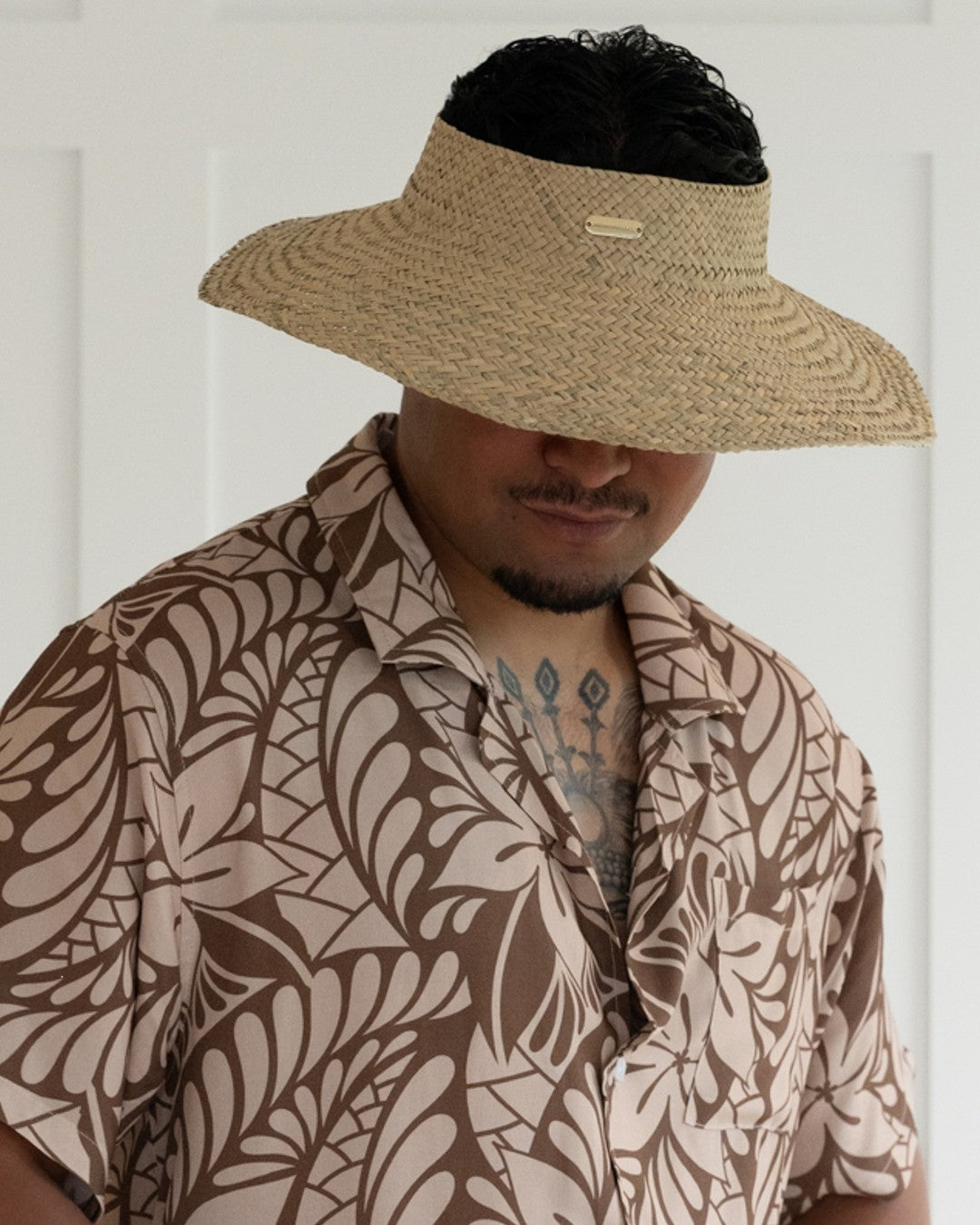 Person wearing a straw visor and patterned shirt against a white background