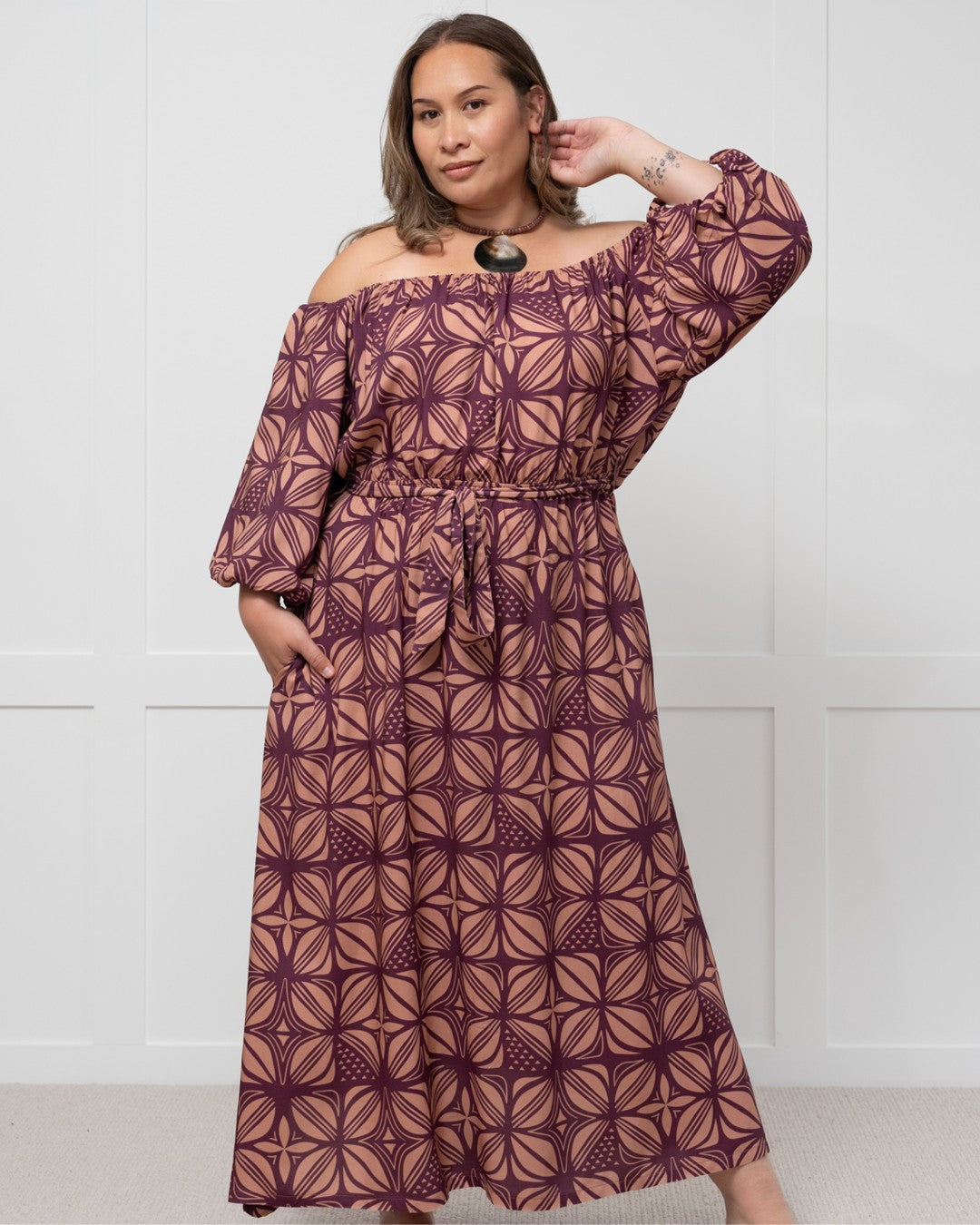 Woman wearing a patterned island dress against a white wall