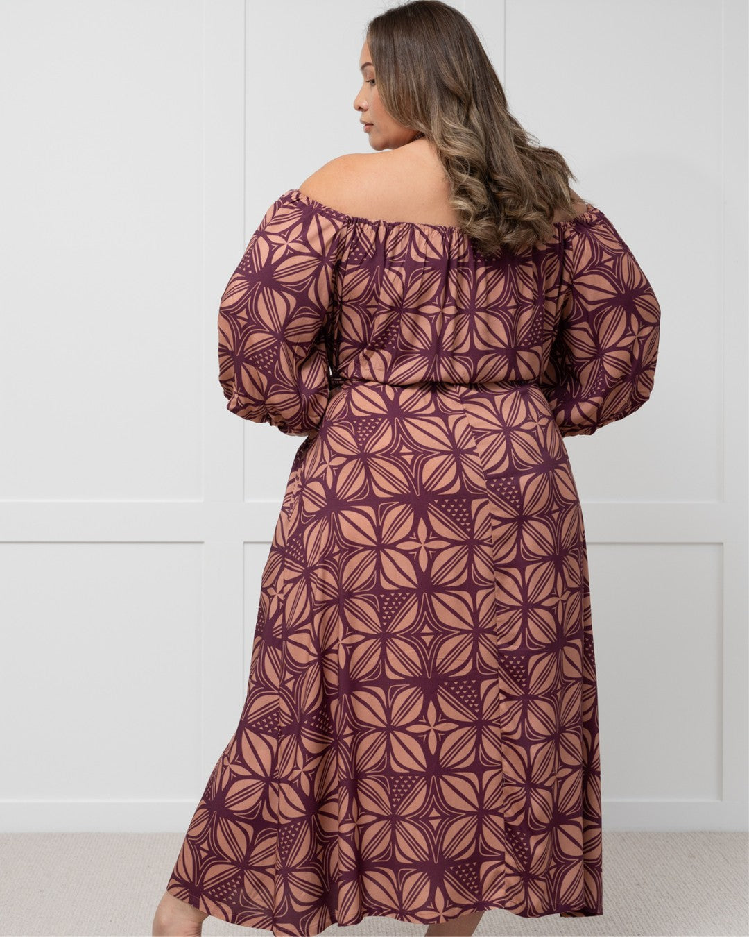 Woman wearing a patterned island dress against a white wall
