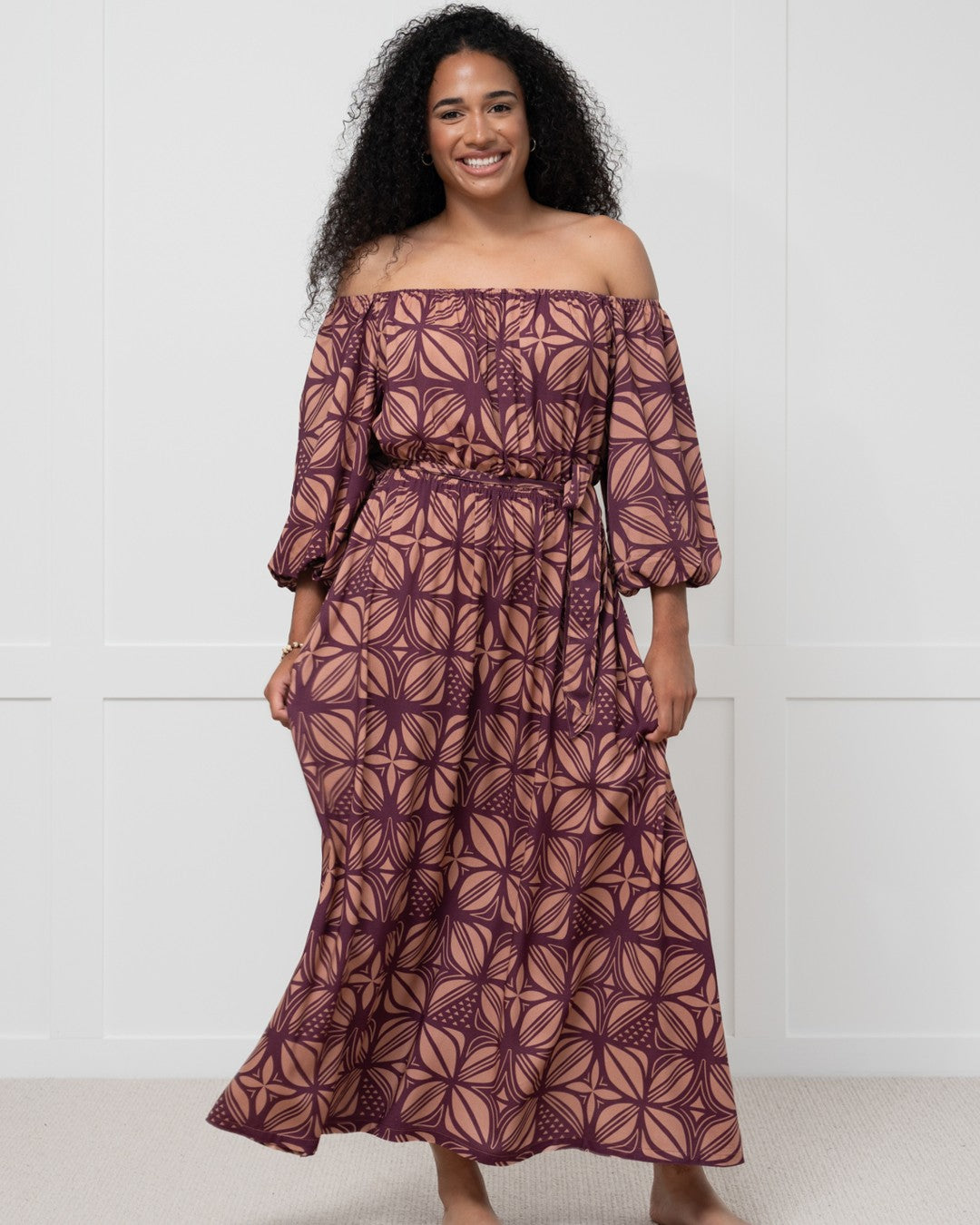 Woman wearing a patterned island dress against a white wall